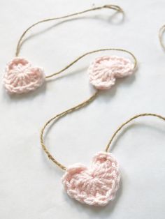 three crocheted hearts hanging from string on a white tablecloth with twine