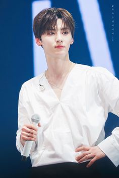 a young man holding a microphone while standing next to a blue wall and wearing a white shirt