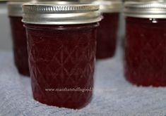 four jars filled with red liquid sitting on top of a blue cloth covered tablecloth