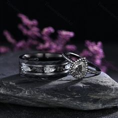 two wedding rings sitting on top of a rock with purple flowers in the back ground