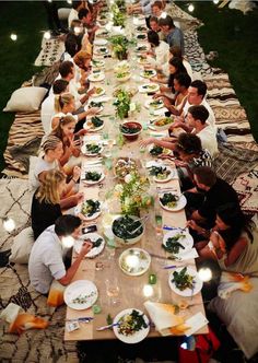 a group of people sitting at a long table with plates and bowls of food on it