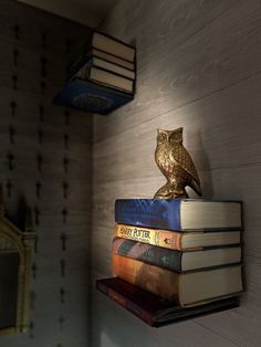 an owl figurine sitting on top of books in a corner next to a mirror