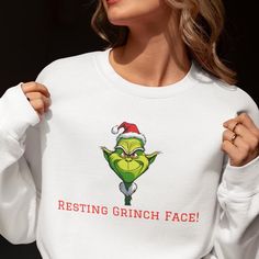 a woman wearing a grin face sweatshirt with the words resting grin face printed on it