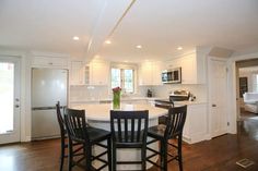 a kitchen with white cabinets, black chairs and a center island in the middle of the room