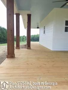 an empty porch with wooden floors and ceiling fan on the side of the house in front of it