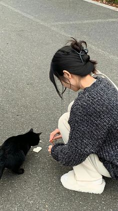 a woman kneeling down next to a black cat