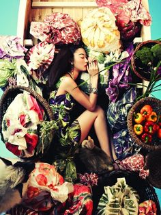 a woman sitting on top of a pile of fruit and vegetables next to a basket