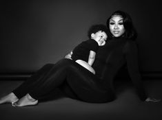 a woman sitting on the ground holding a baby in her lap and posing for a black and white photo