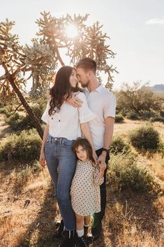 a man and woman standing next to each other in front of a cactus tree with the sun shining on them