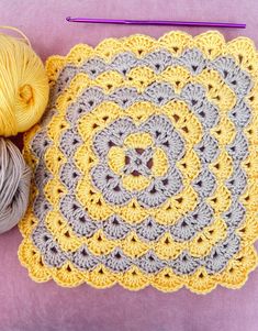 a crocheted square with yarn next to it on a purple surface and two skeins of yarn in the background