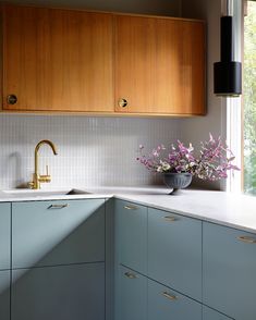 a kitchen with wooden cabinets and white counter tops, flowers in a bowl on the sink