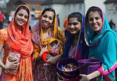 three women in colorful sari holding buckets and smiling at the camera while standing next to each other