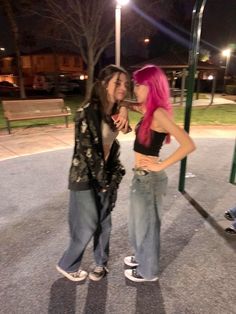 two young women standing next to each other in front of a swing set at night