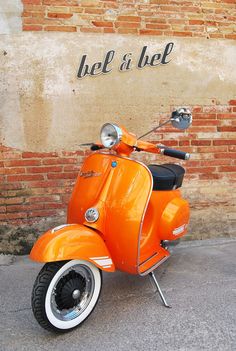 an orange scooter is parked in front of a brick wall