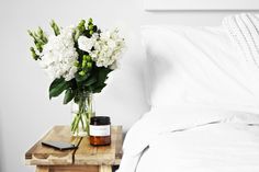 a vase with white flowers on a small wooden table next to a laptop and phone