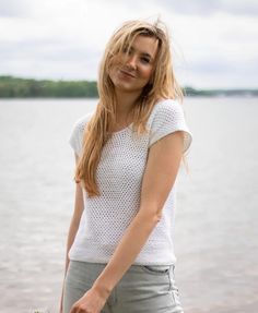 a woman standing next to the water holding a frisbee in one hand and looking at the camera