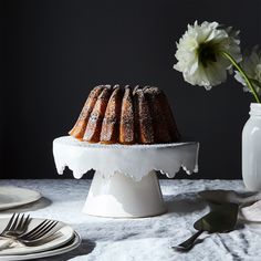 a bundt cake sitting on top of a table next to a white vase filled with flowers