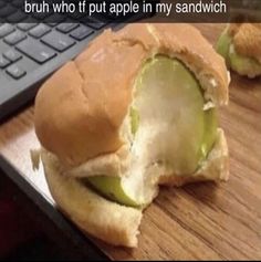 a half eaten sandwich sitting on top of a wooden table next to a laptop computer