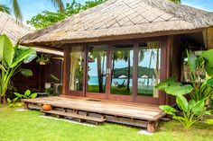 a wooden bench sitting in front of a hut on top of a lush green field