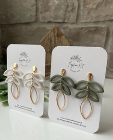 two pairs of earrings with leaves hanging from them on top of a table next to a brick wall