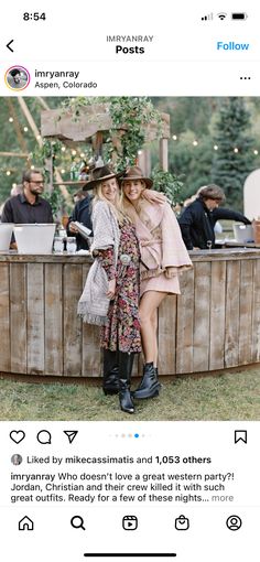 two women are sitting at a bar in the middle of an outdoor area with people standing around