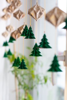 an origami christmas tree mobile hanging from a window in front of a potted plant