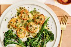 a white plate topped with scallops and broccoli on top of a wooden table