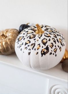 two white pumpkins sitting on top of a mantle with gold foil decorations around them