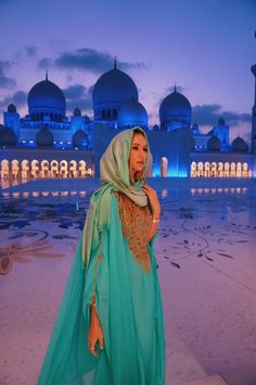 a woman standing in front of a blue building at night with her head scarf draped over her shoulders