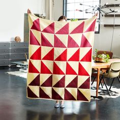 a woman holding up a red and white quilt in the middle of a living room