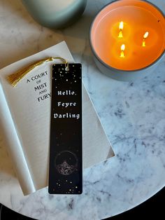 a bookmark sitting on top of a marble table next to a lit candle and cup