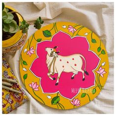 a yellow and pink plate with a cow painted on it next to a potted plant