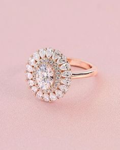 an oval shaped diamond ring with halos in the center on a pink background,