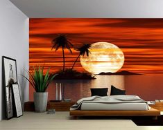 a bedroom with a large bed and palm trees on the shore in front of an orange sunset