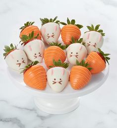 a white cake plate topped with chocolate covered strawberries and carrots decorated to look like faces