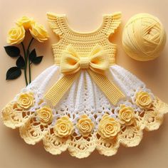 a crochet baby dress with yellow roses next to it