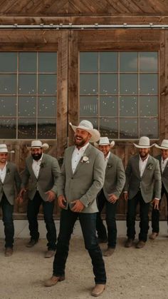 a group of men standing next to each other in front of a wooden building wearing cowboy hats