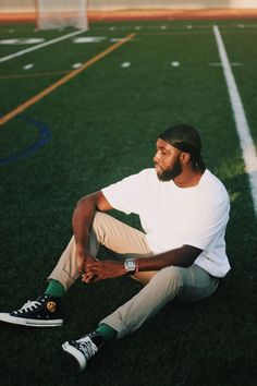 a man sitting on the ground in front of a soccer goal wearing a white shirt and khaki pants