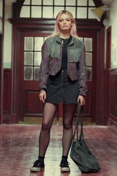 a woman standing in an empty building holding a bag and wearing tight black stockings with her legs crossed