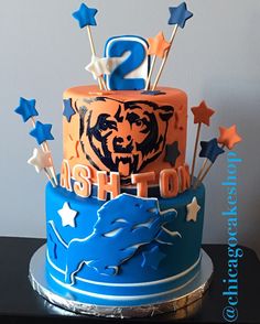 a two tiered cake decorated with blue, orange and white icing has the number 2 on it