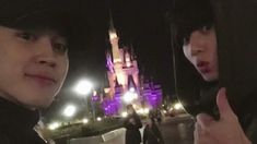 two young men standing next to each other in front of a large castle at night