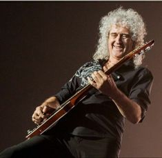 a man with long white hair holding a guitar in his right hand and smiling at the camera