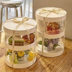 two round boxes with flowers and gifts in them on top of a wooden table next to a bar stool