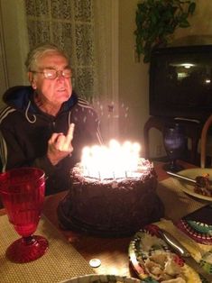 an old man sitting at a table with a cake in front of him that has lit candles on it