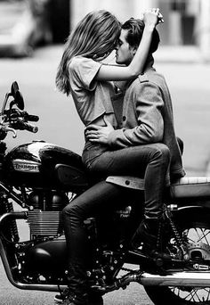 a man and woman sitting on top of a motorcycle kissing in the middle of the street