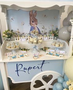 a blue and white dessert table with cupcakes on it's shelf, balloons in the background