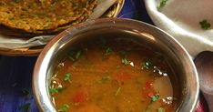 a metal bowl filled with soup next to some bread on a blue table cloth and two spoons