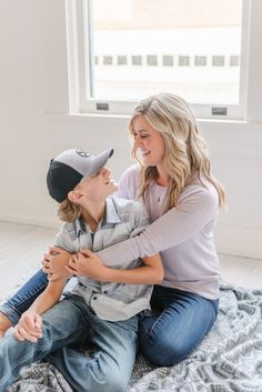 a mother and her son sitting on the floor laughing at each other while they both wear baseball caps