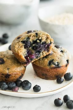 two blueberry muffins on a white plate with some blueberries around it