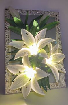 a white flower sitting in front of a mirror on top of a table next to a wall